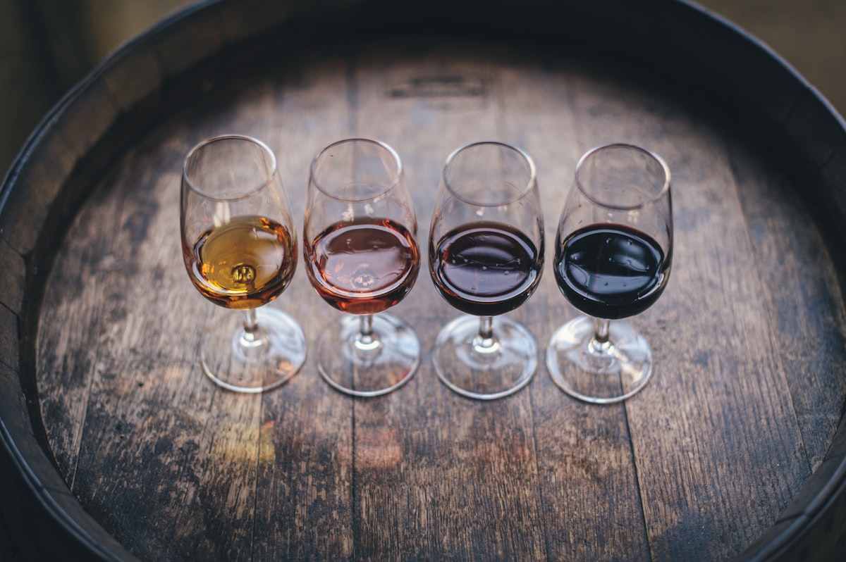 Four wine glasses with different wines lined up on a wooden barrel for tasting